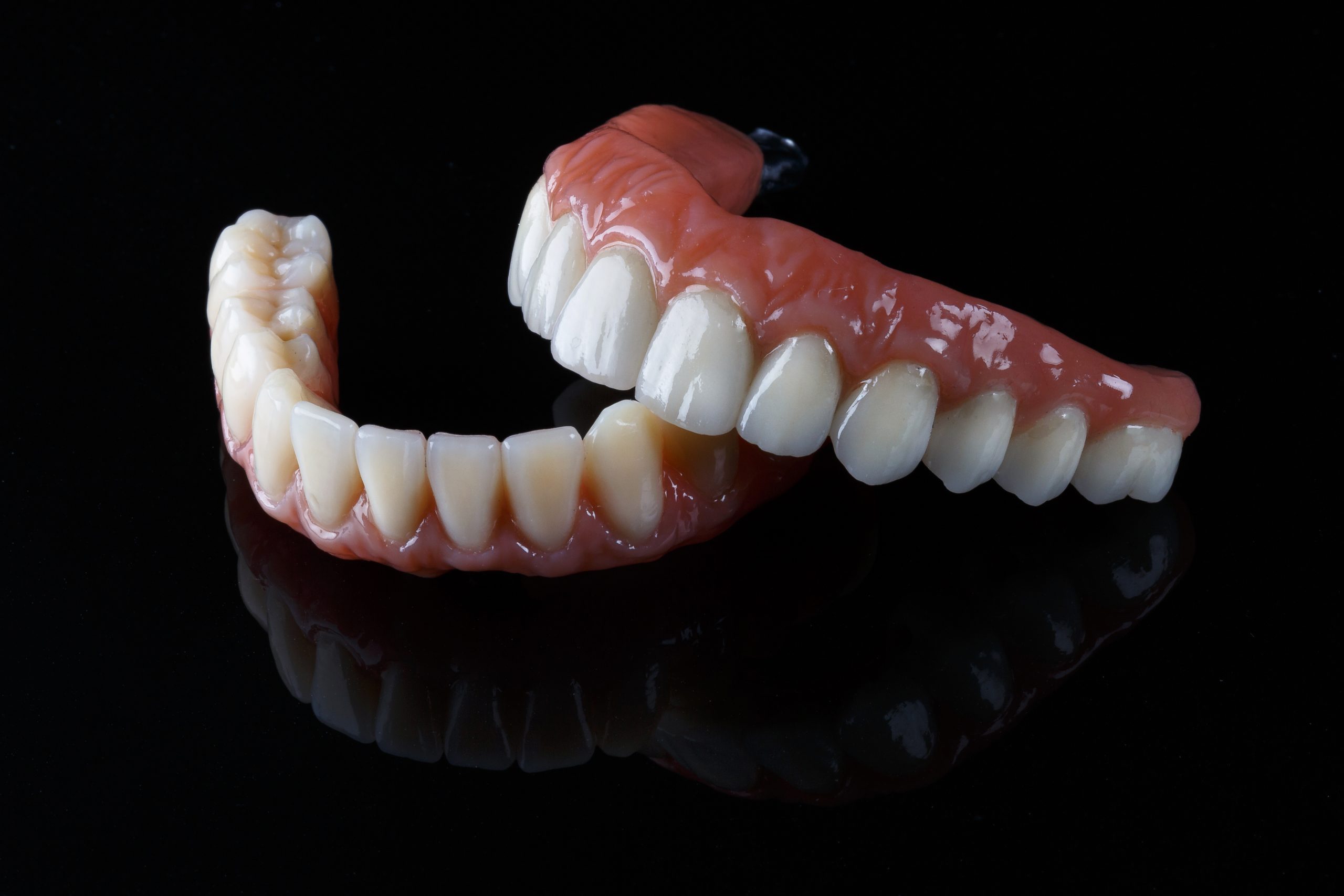 ceramic prosthesis with artificial gums, upper and lower jaw on black glass